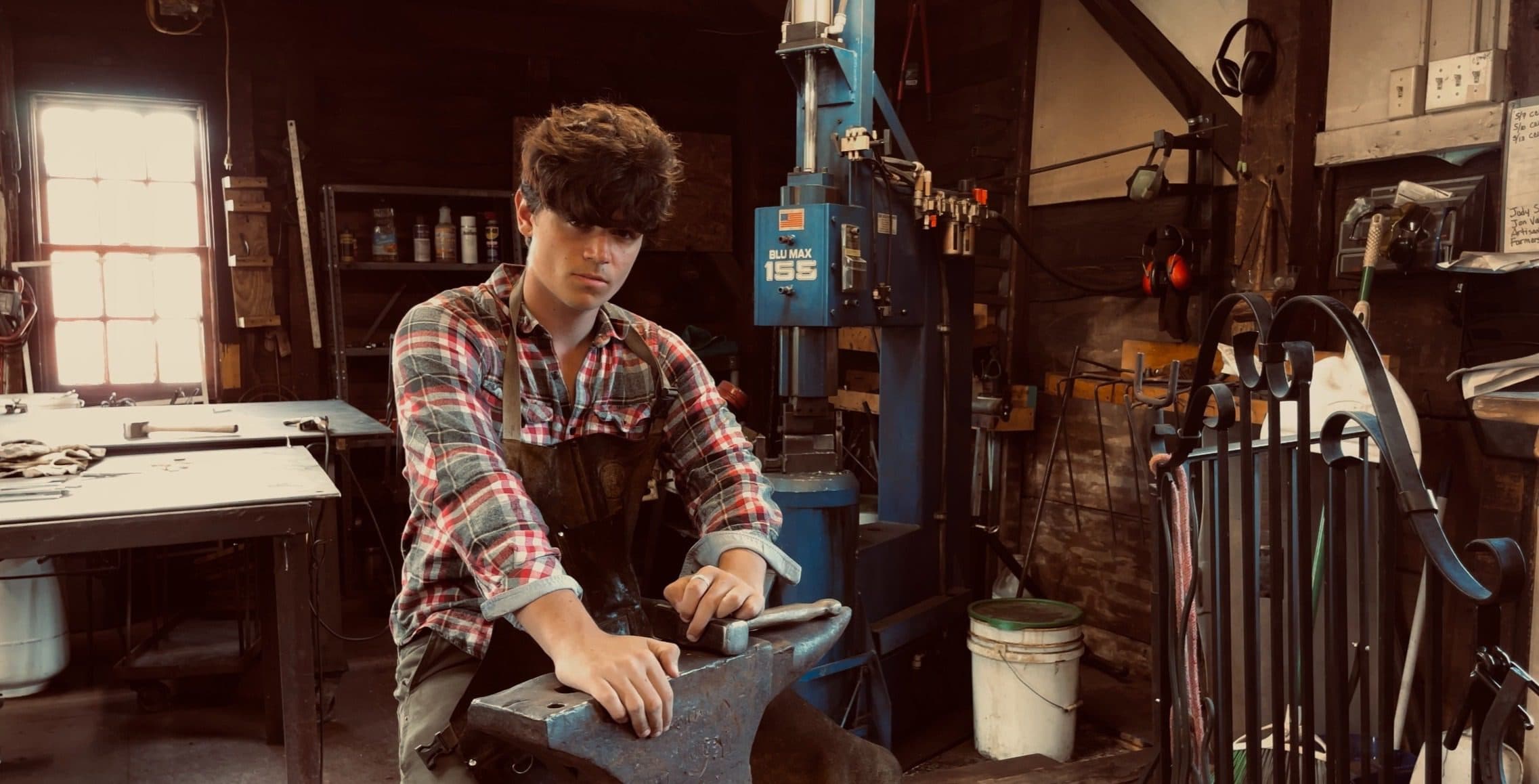 Judson at the anvil in the shop he built, stone wall behind him