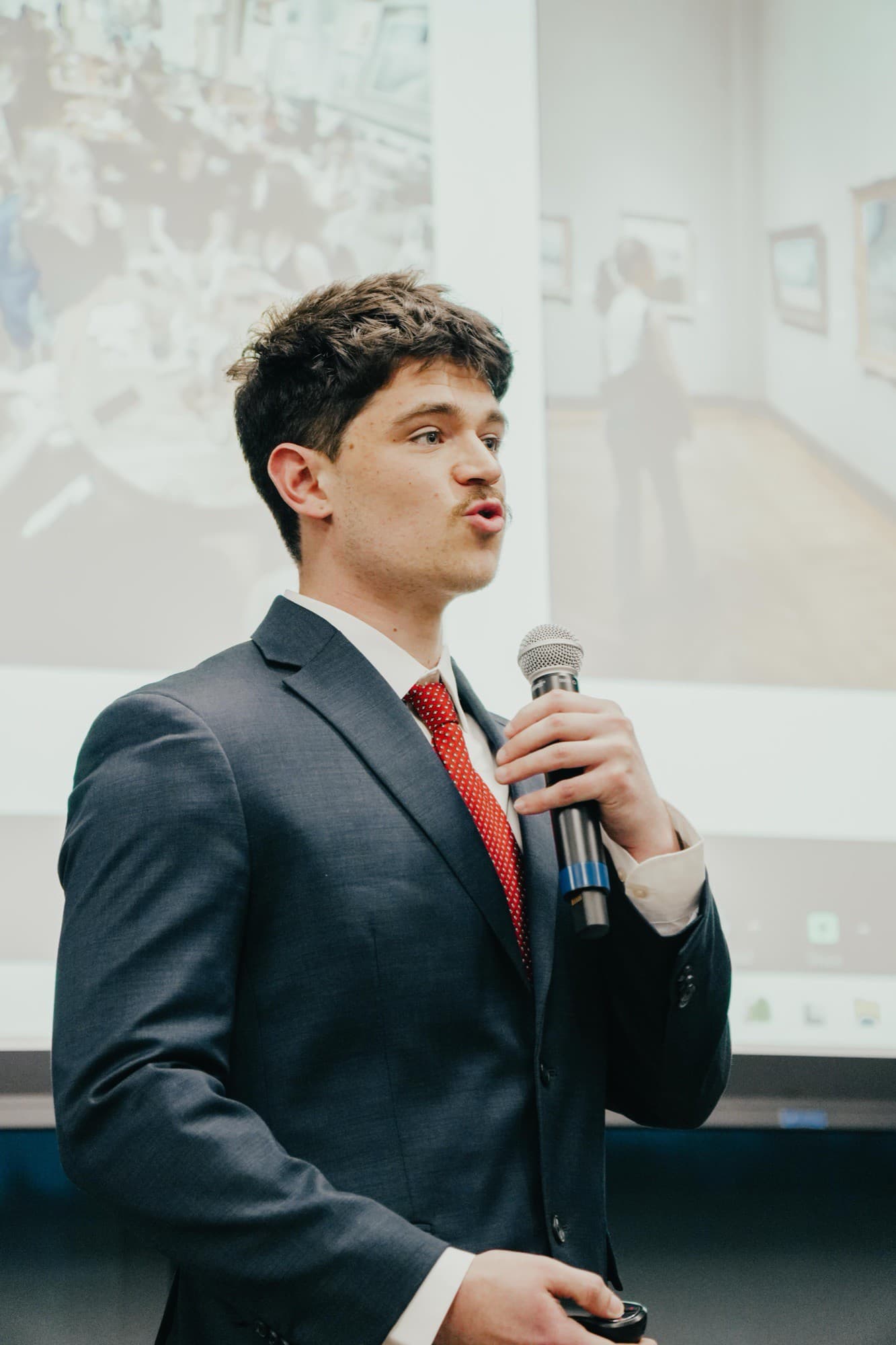 Judson Dunne presenting Locava on stage in a navy suit, the pitch deck projected behind him