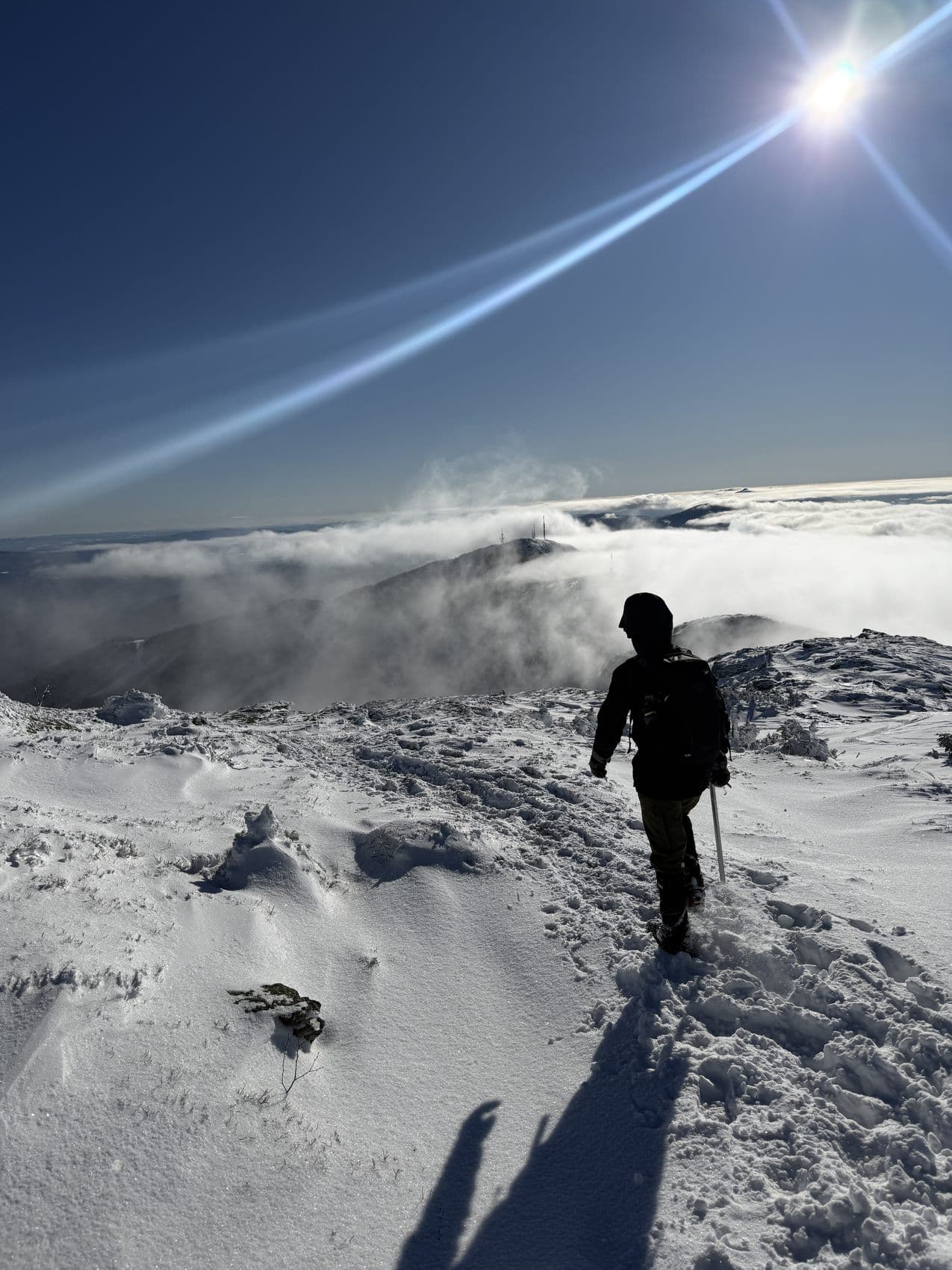 A climber silhouetted on a snow ridge against the sun