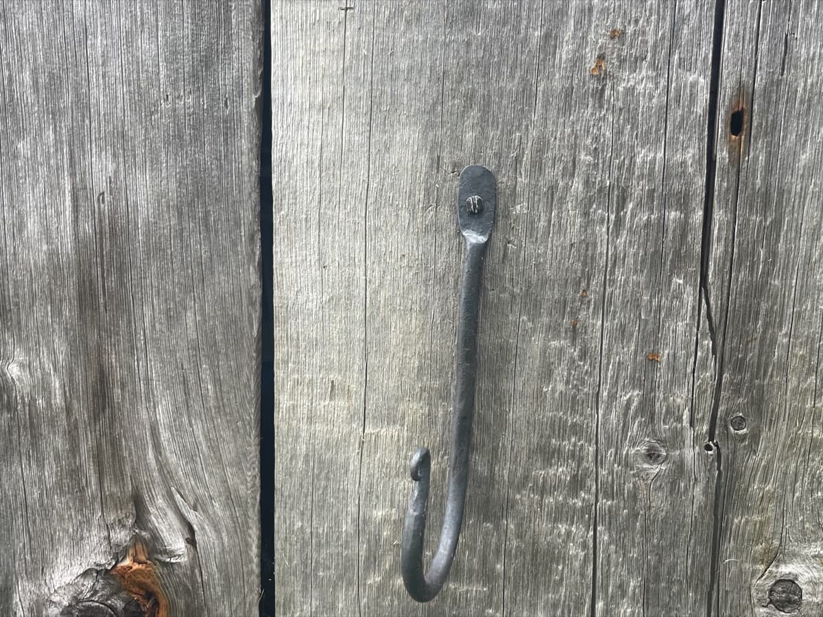 A hand-forged hook mounted on weathered barn board