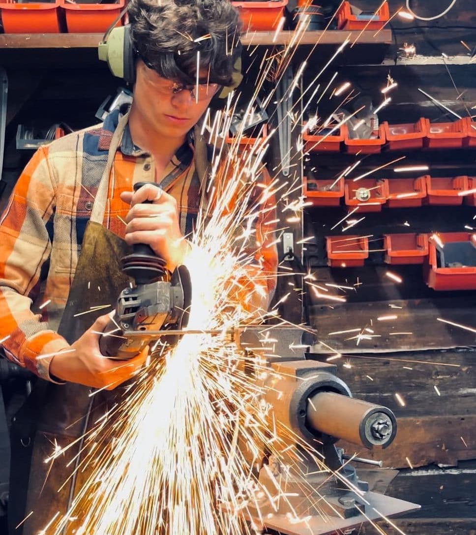 Judson Dunne grinding a forged piece, sparks off the wheel, inside Misty Mountain Forge