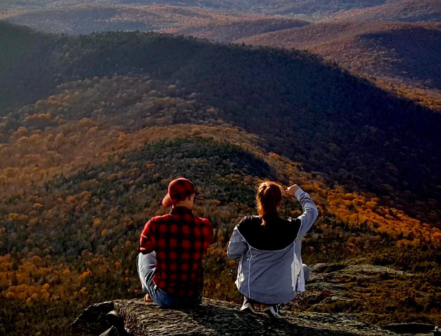Two people sitting on a rock outcrop above Vermont hills in fall